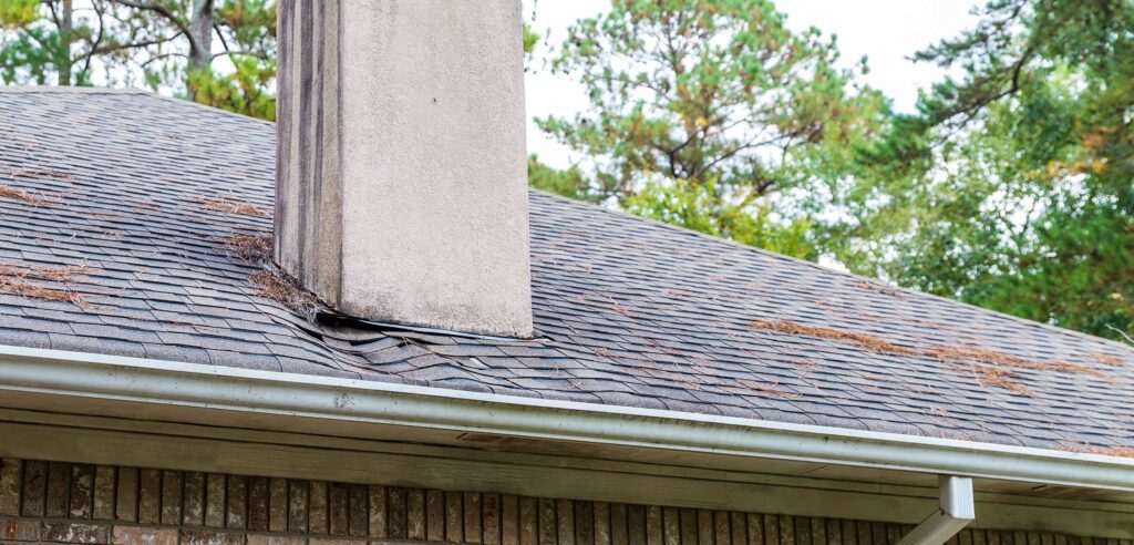 8 Common Causes of a Leaky Roof - Guns N Hoses Roofing Sagging shingles near chimney on roof.
